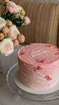 a pink cake sitting on top of a table next to a vase filled with flowers