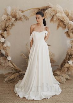 a woman in a white wedding dress standing next to a large wreath with feathers on it