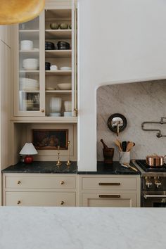 a kitchen with white cabinets and marble counter tops, gold pulls on the cupboards