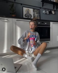 a woman sitting on the floor in front of an open laptop and holding a drink