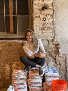 a woman sitting on top of stacks of boxes next to a brick wall and window