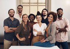 a group of people standing together in front of a white table with their arms crossed