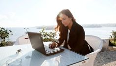 a woman sitting at a table with a laptop computer on her lap and looking at the screen