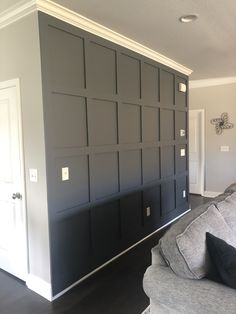 a living room with black paneling and white trim on the walls, along with a gray couch