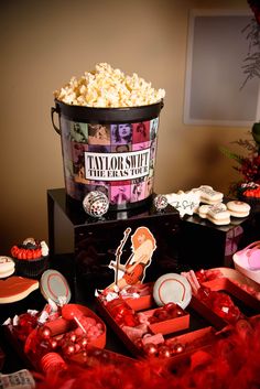 a bucket full of popcorn sitting on top of a table next to cupcakes