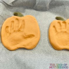 two pumpkin shaped cookies with hand prints on them