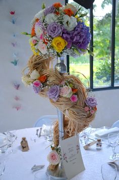 an arrangement of flowers on top of a table in a room with windows and chairs