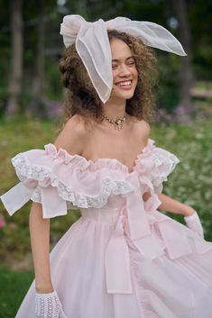 a woman in a pink dress and white bonnet smiles at the camera while standing outside