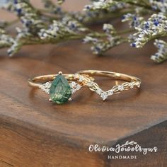 two gold rings with green and white stones sitting on top of a wooden table next to lavender flowers