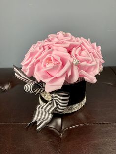 a bouquet of pink roses sitting on top of a brown leather chair with black and white ribbon