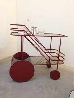 a red metal cart with drinks on it in a white walled room next to a wall