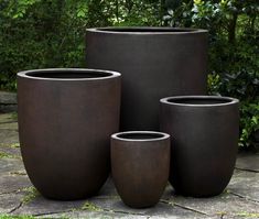 four large pots sitting on top of a stone floor next to green bushes and trees