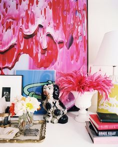 a table topped with books and vases filled with flowers next to a pink painting