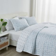 a bed with blue and white quilted bedspread on top of it next to a window