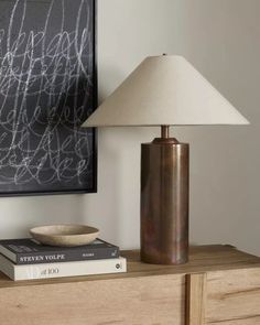 a lamp sitting on top of a wooden table next to a book and a bowl