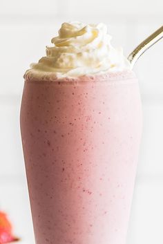 a smoothie with whipped cream on top in a tall glass next to strawberries