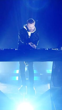 a man standing in front of a blue light on top of a stage with his hands together