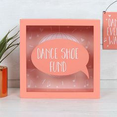 a pink box with a speech bubble saying dance shoe fund on it next to a potted plant