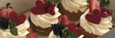 several cupcakes with white frosting and strawberries on top are in a box