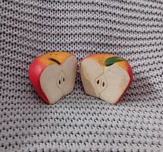 two apples with faces carved into them sitting on a gray knit surface next to each other