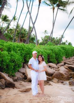 a man and woman standing on the beach in front of palm trees with their arms around each other