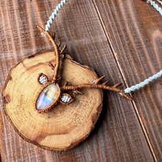 a tree slice with a pendant on it sitting on top of a wooden table next to a beaded necklace