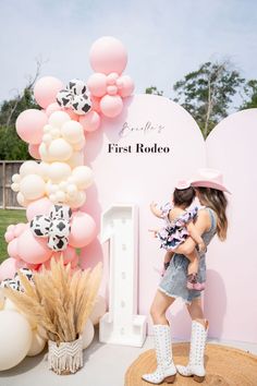 a woman holding a baby in her arms next to a pink and white balloon arch