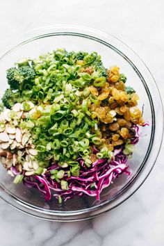 a glass bowl filled with broccoli, red cabbage and almonds on top of a marble counter