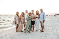 a group of people standing on top of a sandy beach next to the ocean at sunset