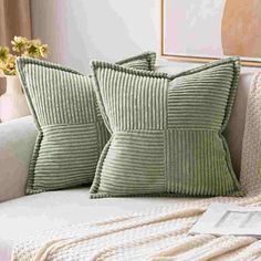 two green pillows sitting on top of a white couch next to a vase with flowers