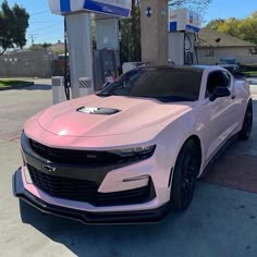 a pink chevrolet camaro is parked at a gas station