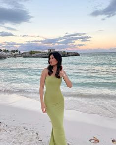 a woman is standing on the beach in a green dress and looking off into the distance