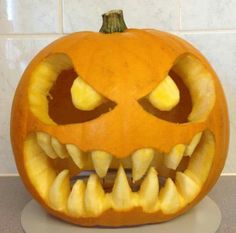 a carved pumpkin with large teeth on it's face is displayed in front of a white tile wall