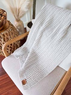 a white knitted blanket sitting on top of a wooden chair next to a potted plant