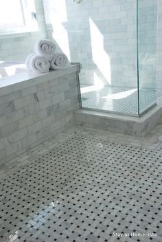 a white tiled bathroom with two rolls of towels on the edge of the bathtub