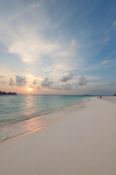 the sun is setting on an empty beach with people walking in the sand and water