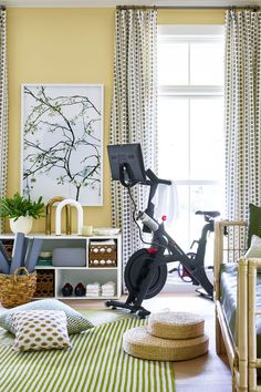 a room with yellow walls, green and white striped curtains, an exercise bike in the foreground