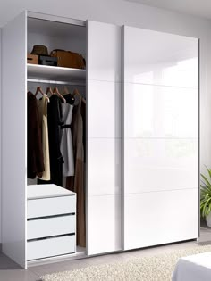 a white closet with clothes hanging on the shelves and drawers in front of it, next to a bed