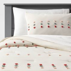 a bed with white sheets and red flowers on the comforter, along with two pillows