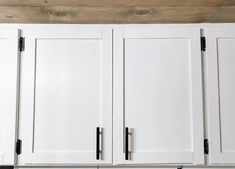 white kitchen cabinets with black handles and knobs on the bottom, against a wooden ceiling