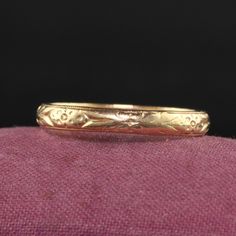 a gold wedding band sitting on top of a pink fabric covered surface with black background