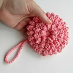 a pink crocheted object being held by someone's hand on a white surface