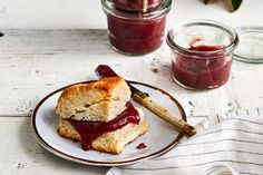 two jam sandwiches are on a plate with spoons and jar of jelly in the background