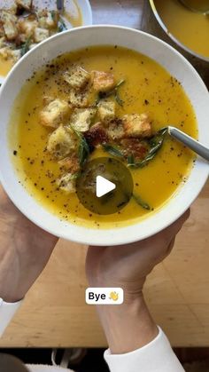 two hands holding a bowl of soup with bread and vegetables