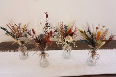 three vases filled with dried flowers on top of a white cloth covered tablecloth