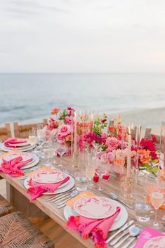 the table is set with pink and yellow flowers in vases, napkins, and plates