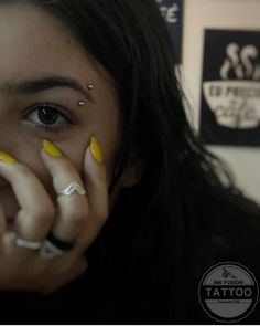 a woman with yellow and white nail polish holding her hands to her face while looking at the camera