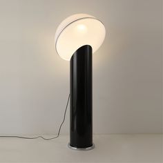 a black and white lamp with a round light on it's base next to a wall