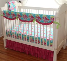 a white crib with pink, blue and green ruffled bedding on it