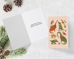 two greeting cards with dinosaurs on them and pine cones around the edges, one is for christmas